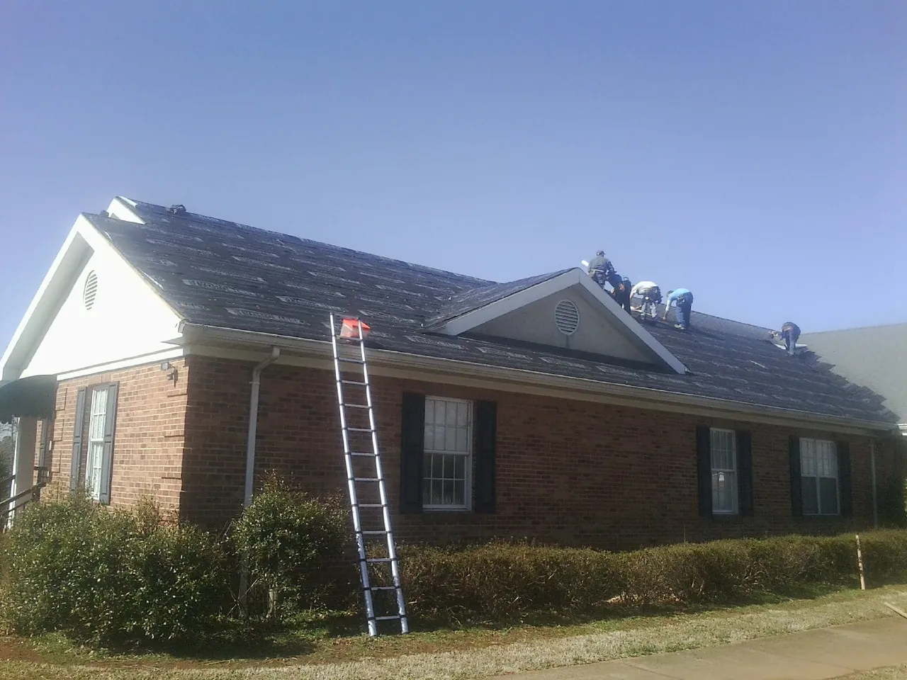 Crew tearing shingles off a brick ranch roof with a ladder set — Emergency Roof Repair work by our crew in Clarksville