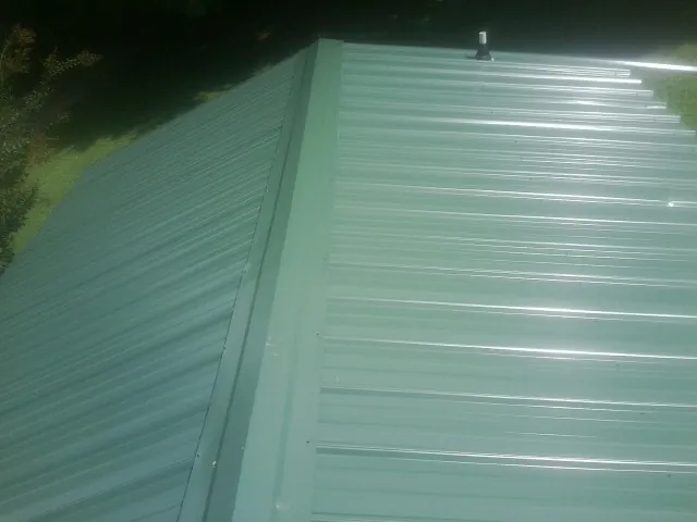 New green metal panels meeting at the ridge of a roof — Flat Roof Repair work by our crew in Clarksville